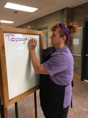 Mrs. Becky, staff at West Middle School, writing the lunch menu for the day.